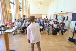 Beate Brieden blickt zu der großen Anzahl an Teilnehmenden. Sie sitzen alle auf Stühlen.