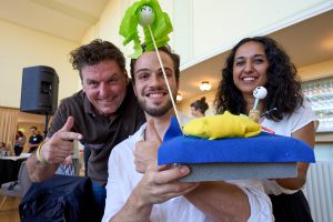 Eine Gruppe präsentiert stolz ihr Modell. Es sind zwei Figuren auf einem blau-gelben Boden. Sie lächeln in die Kamera.